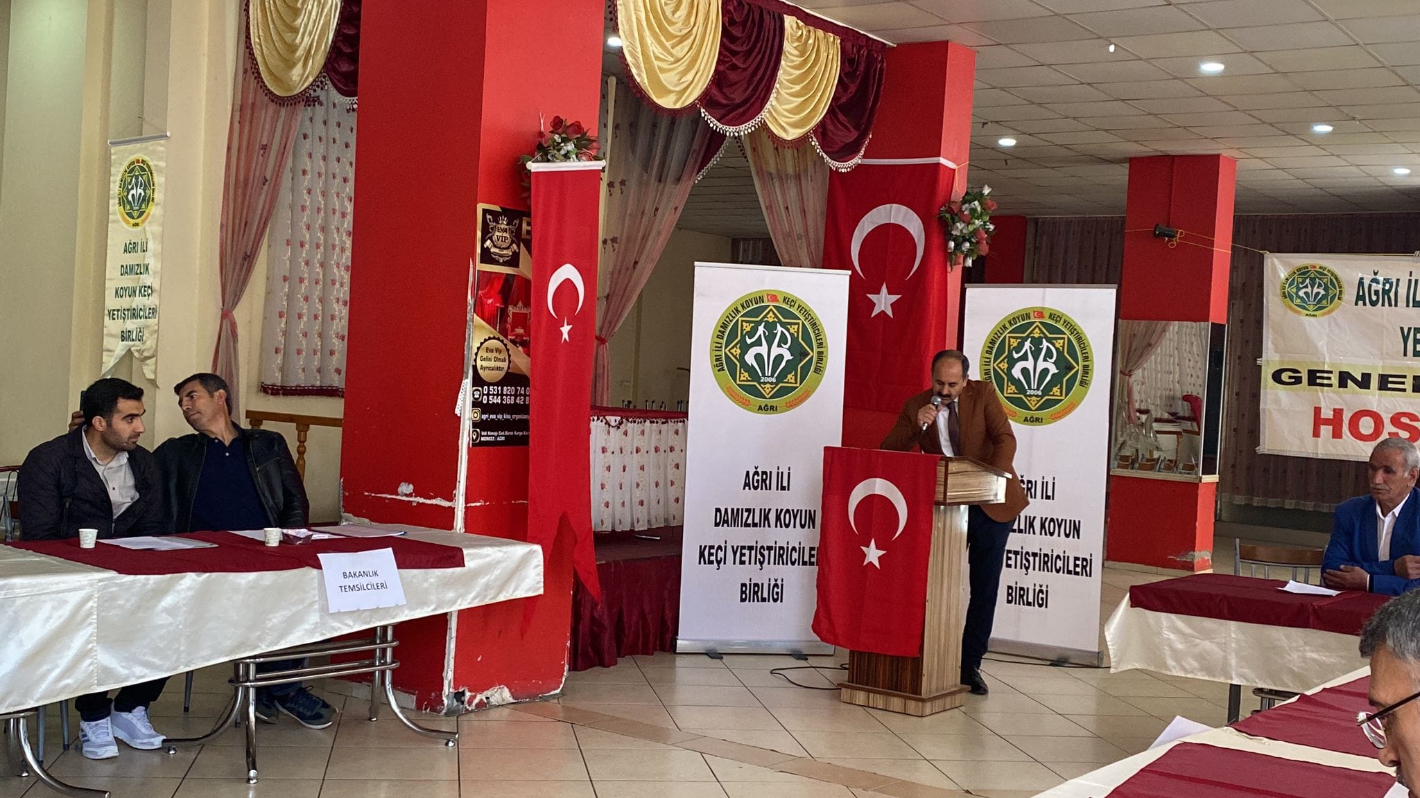 Bir 5 kişi, kürsü ve şunu diyen bir yazı 'แลป AOX IDYON 微使 NEP KETQRAICLaR 税込 已卓料 ส BARANLX TEMSADUN GENE HOS AĞRIİLI DAMIZLIK DAMIZLIKKOYUN KOYUN KEÇİ YETİŞTİRİCİLE BİRLİĞİ RIİLi LIKKOYUN ETİŞTİRİCİLERİ BİRLİĞİ' görseli olabilir